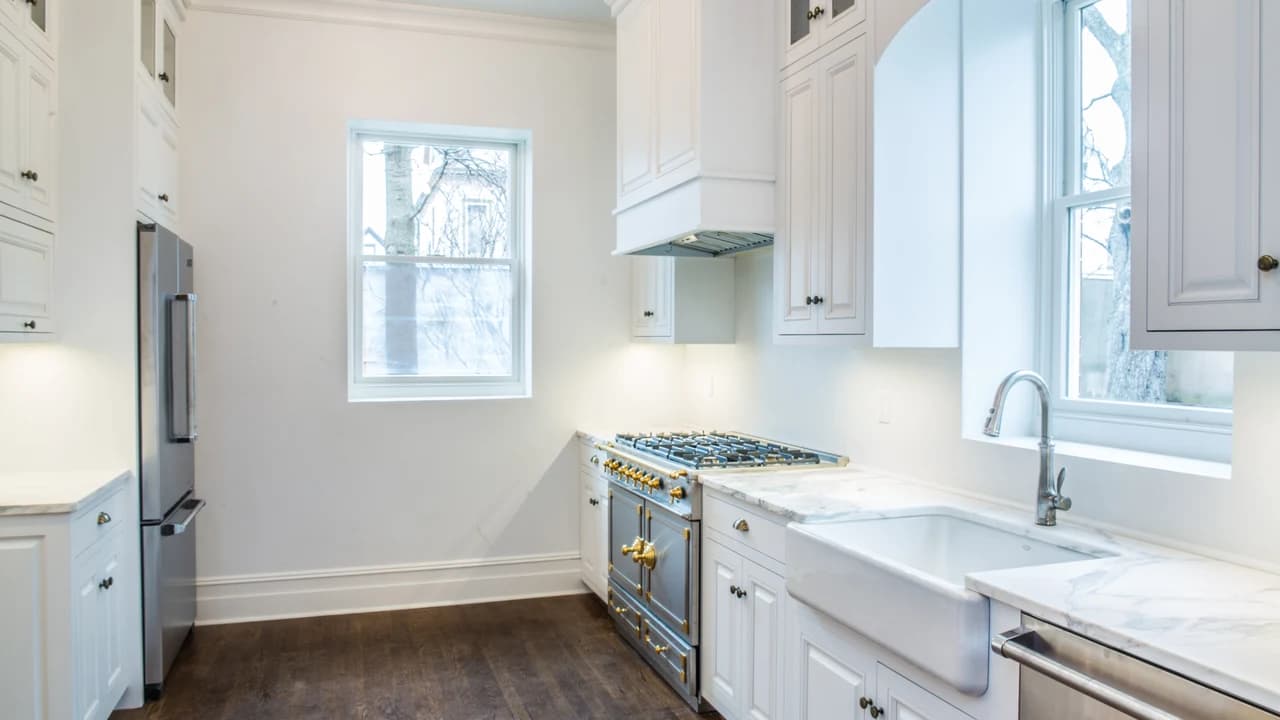 White kitchen with tall cabinetry, a farmhouse sink, a metal range with brass details, and dark wood flooring.
