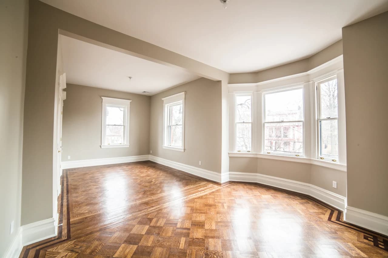 Sunlit adjoining rooms with patterned wood flooring, white trim, and a curved bay of windows.