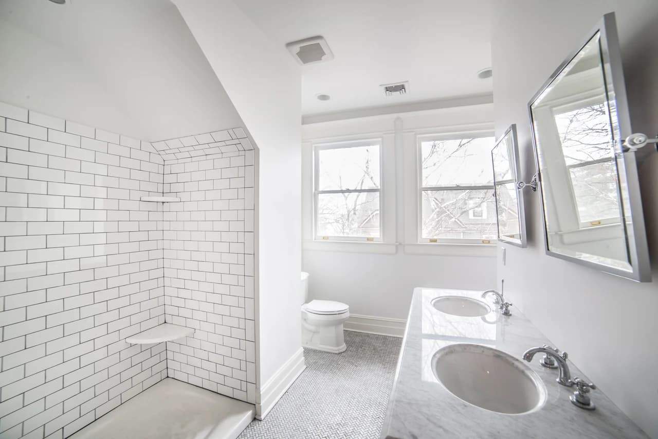 Bright bathroom with a white subway-tile shower, double vanity, mirrored cabinets, and small patterned floor tiles.