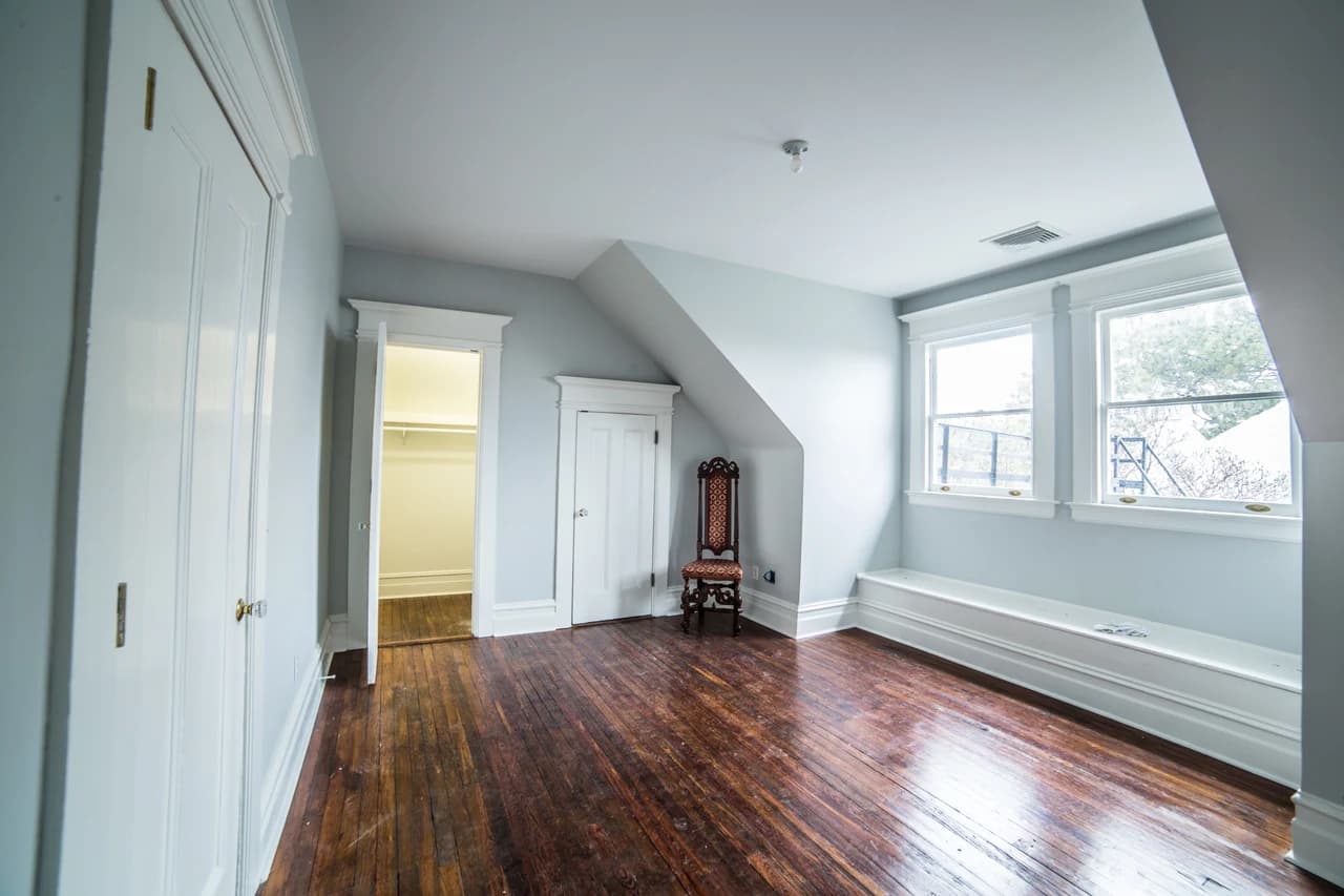 Upper room with pale blue walls, a sloped ceiling, wood flooring, and a window seat beneath paired windows.