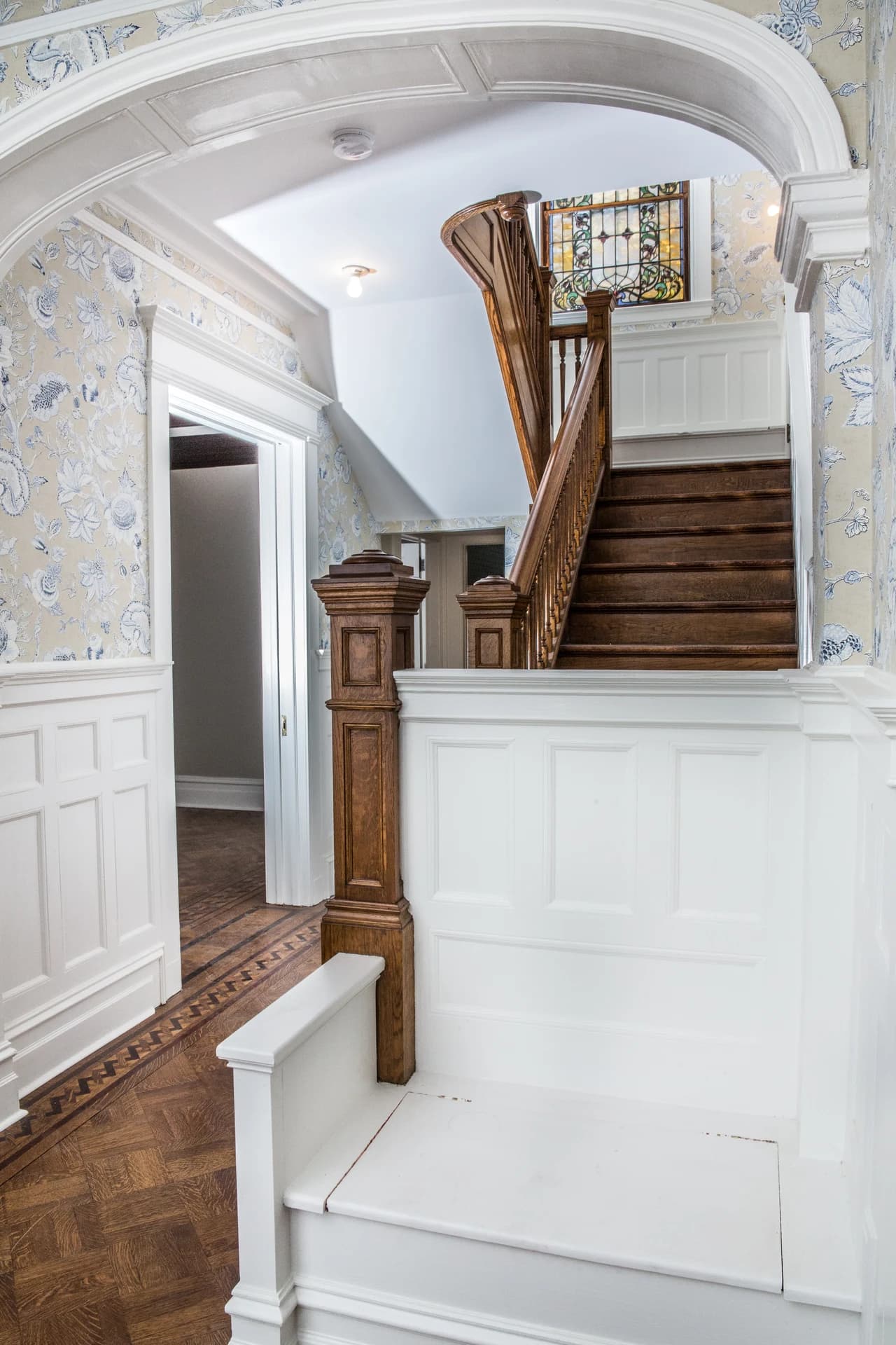 White arched opening framing a wood staircase, stained-glass window, and paneled built-in bench.