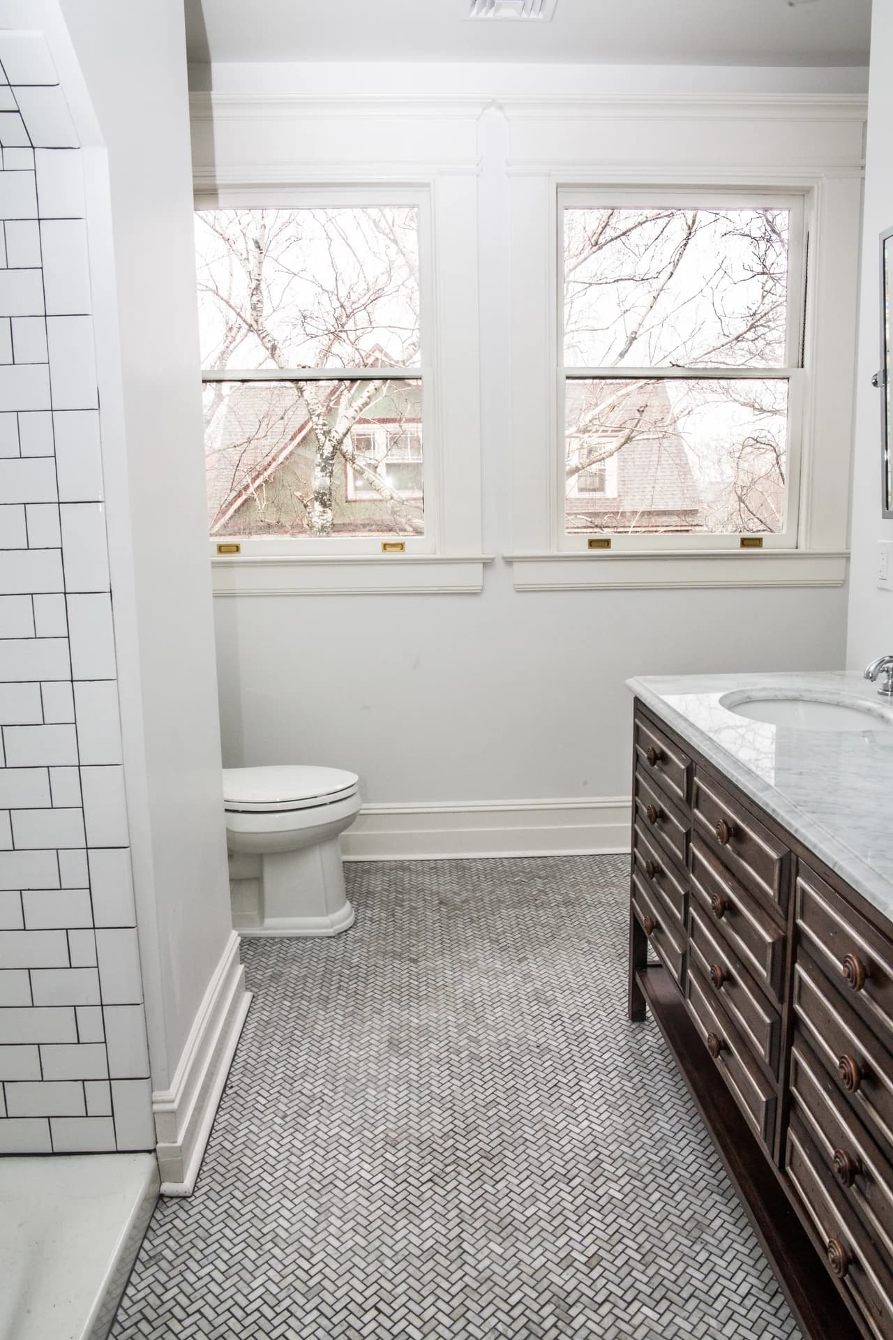 Bathroom with a dark wood vanity, stone countertop, herringbone-pattern floor tile, and two windows.